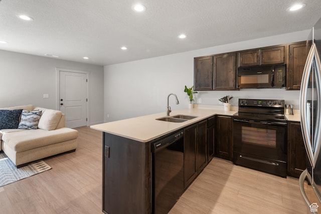 kitchen featuring a sink, light countertops, open floor plan, light wood-type flooring, and black appliances