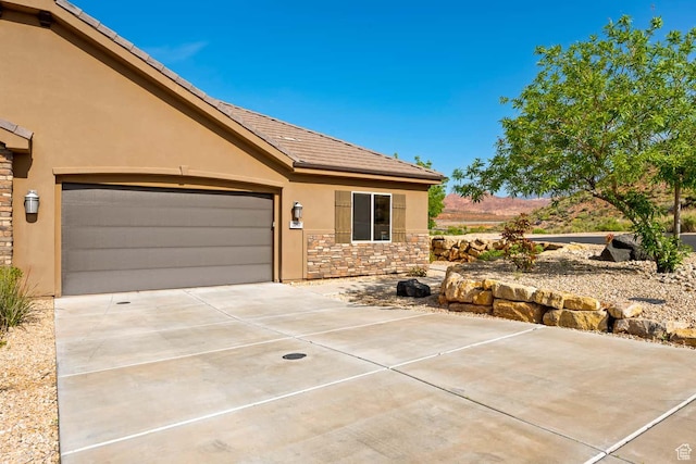 ranch-style house featuring concrete driveway, a garage, stone siding, and stucco siding