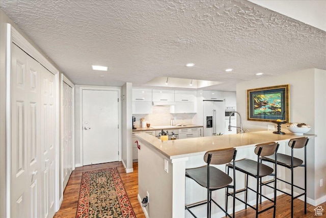 kitchen featuring high end fridge, a breakfast bar, light wood-style floors, white cabinetry, and a peninsula