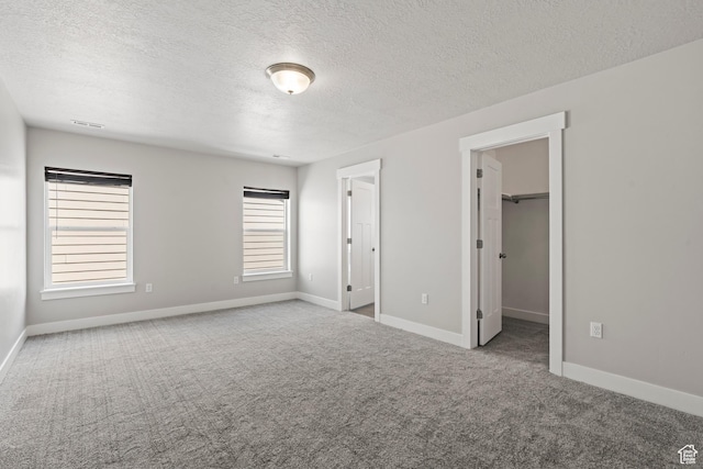unfurnished bedroom with carpet flooring, a walk in closet, a textured ceiling, and baseboards