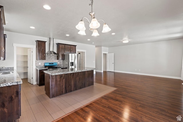 kitchen with wall chimney range hood, dark brown cabinets, appliances with stainless steel finishes, a sink, and a kitchen island