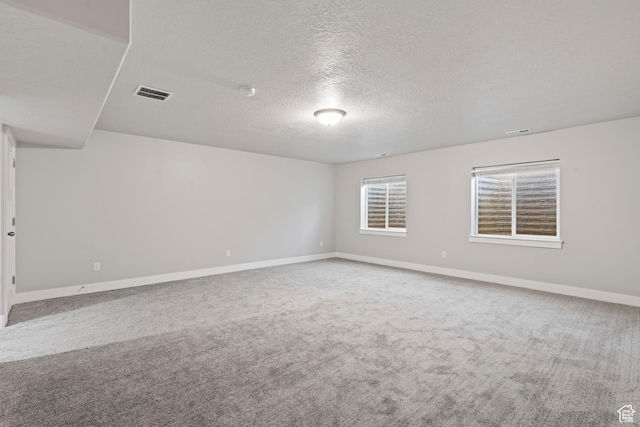 carpeted empty room featuring baseboards, a textured ceiling, and visible vents