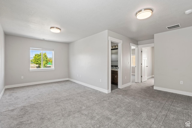carpeted spare room featuring baseboards, a textured ceiling, and visible vents
