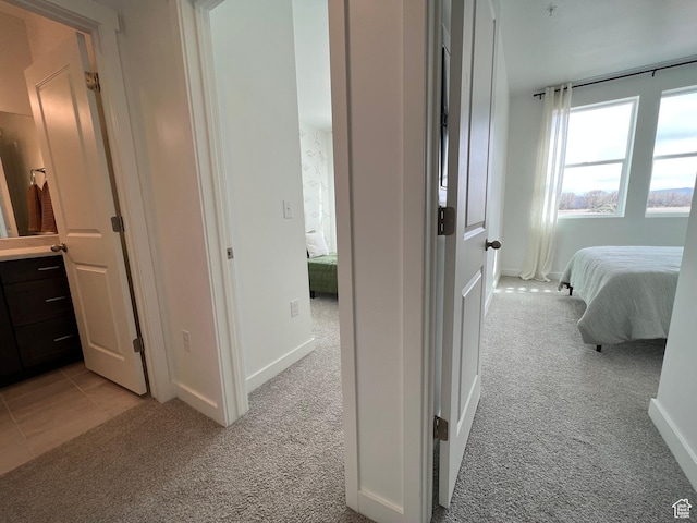 corridor with baseboards and light colored carpet