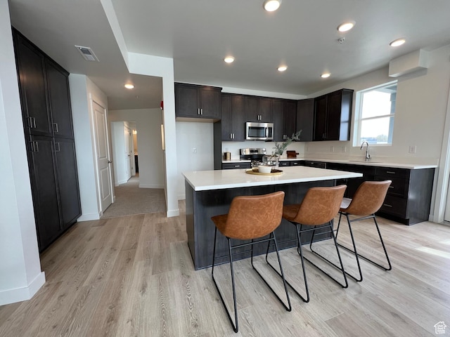kitchen with a sink, light countertops, stainless steel appliances, light wood-type flooring, and a kitchen island