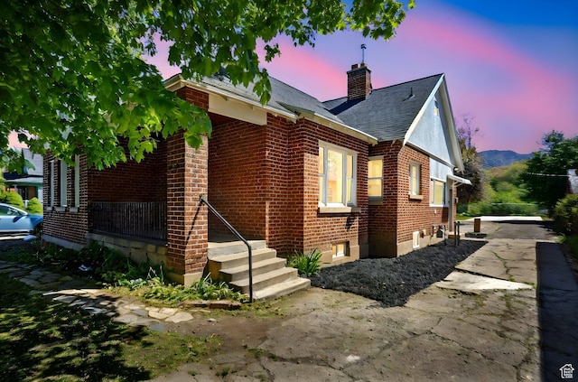 exterior space with roof with shingles, a chimney, and brick siding