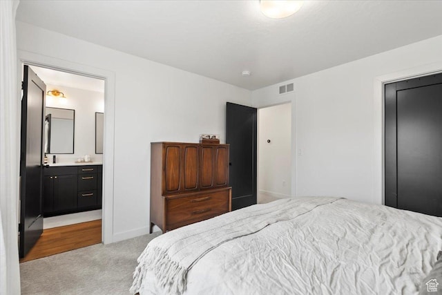 bedroom with visible vents, baseboards, ensuite bathroom, and light carpet