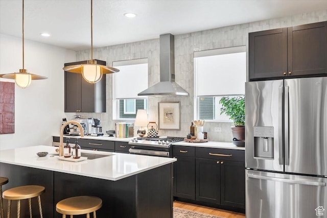 kitchen featuring a kitchen bar, range, a sink, stainless steel fridge, and wall chimney exhaust hood