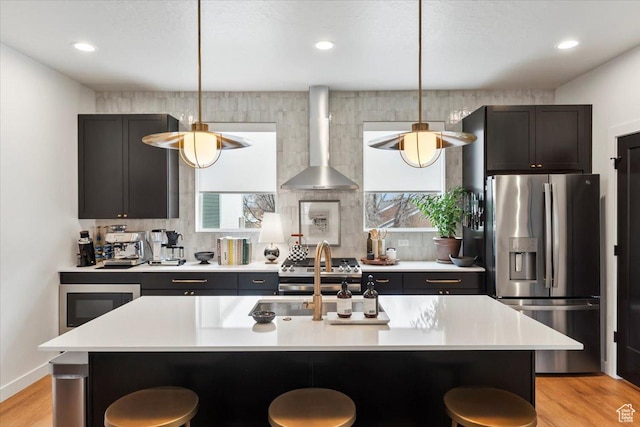 kitchen with light countertops, wall chimney exhaust hood, a kitchen bar, and stainless steel appliances