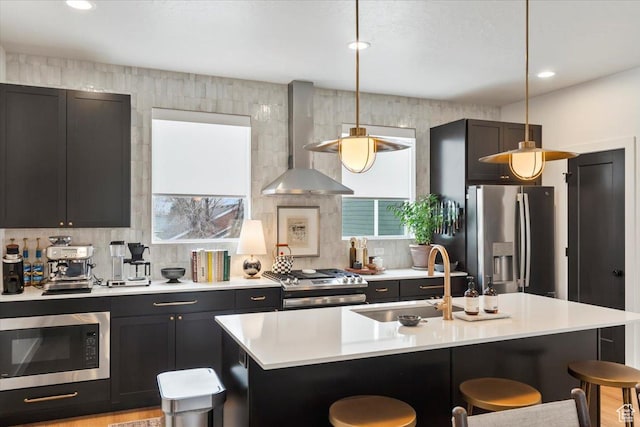 kitchen with appliances with stainless steel finishes, a sink, a breakfast bar area, light countertops, and wall chimney exhaust hood