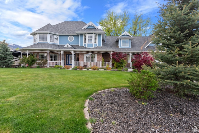 victorian home with a porch, brick siding, a shingled roof, and a front lawn