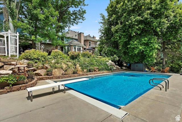 outdoor pool with a diving board and a patio area