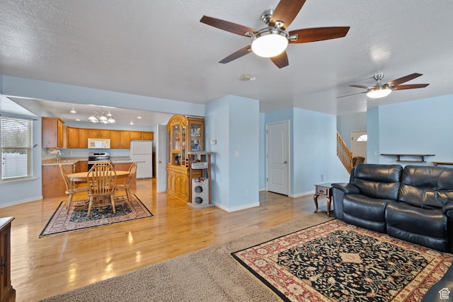 living room featuring baseboards, ceiling fan with notable chandelier, and light wood-style floors