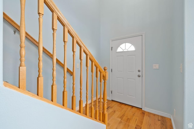 entryway with stairs, baseboards, light wood-style flooring, and a towering ceiling