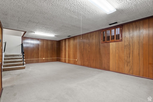 finished below grade area featuring wood walls, carpet flooring, and stairway