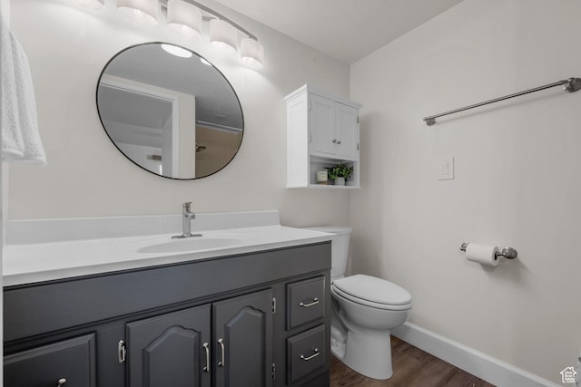 bathroom with toilet, baseboards, wood finished floors, and vanity