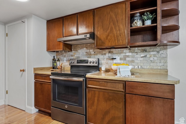 kitchen with tasteful backsplash, light wood-type flooring, stainless steel range with electric stovetop, light countertops, and under cabinet range hood