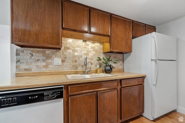 kitchen featuring decorative backsplash, light wood-type flooring, a sink, light countertops, and white appliances