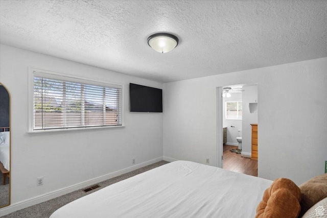 bedroom with connected bathroom, a textured ceiling, visible vents, and baseboards