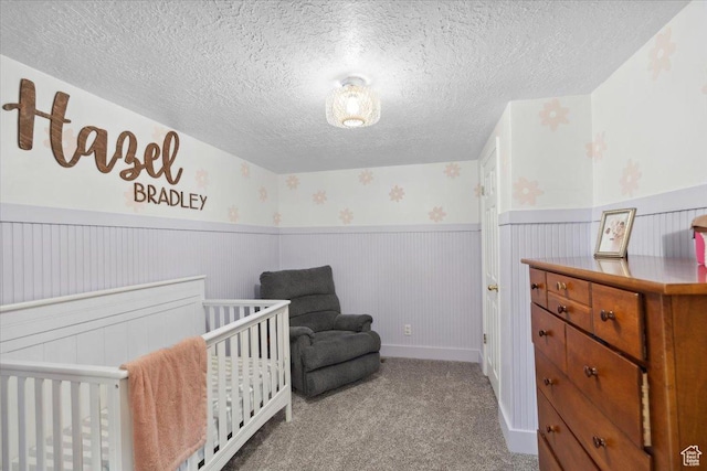 carpeted bedroom with a crib, a textured ceiling, and a wainscoted wall