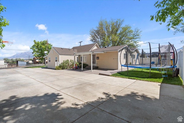 back of property with a shed, a patio area, a trampoline, a mountain view, and an outbuilding