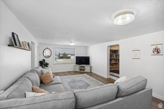 living room with arched walkways, baseboards, a textured ceiling, and dark wood-type flooring