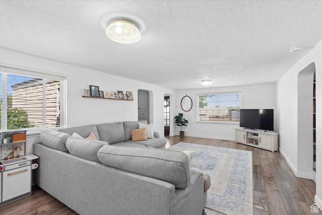 living area with baseboards, arched walkways, a textured ceiling, and wood finished floors