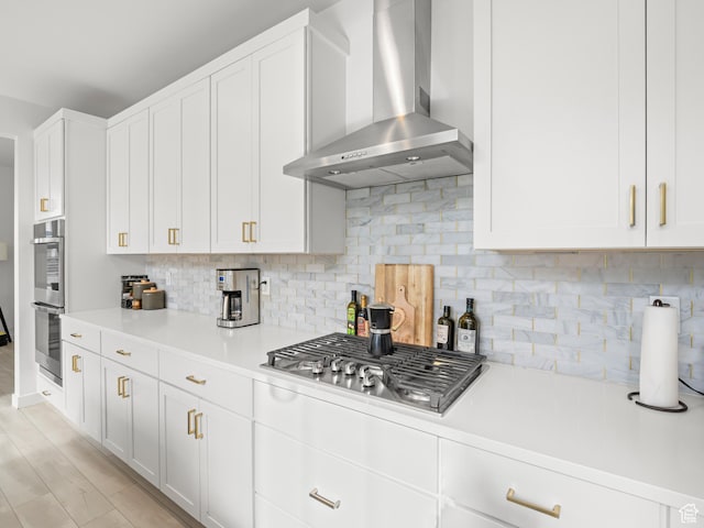 kitchen featuring light countertops, wall chimney exhaust hood, stainless steel appliances, white cabinetry, and decorative backsplash