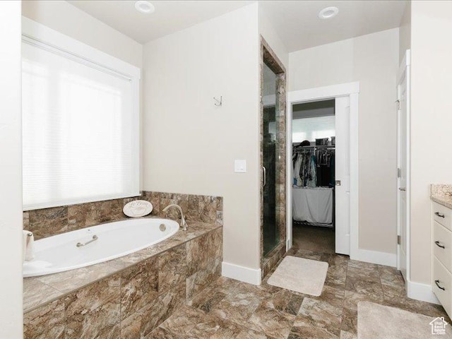 full bathroom featuring a garden tub, vanity, baseboards, a spacious closet, and a shower stall