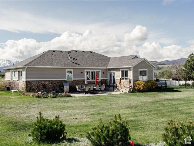 rear view of house with a lawn, a patio area, fence, and stone siding