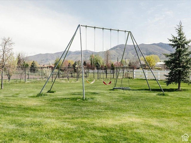 view of playground featuring a lawn, fence, and a mountain view