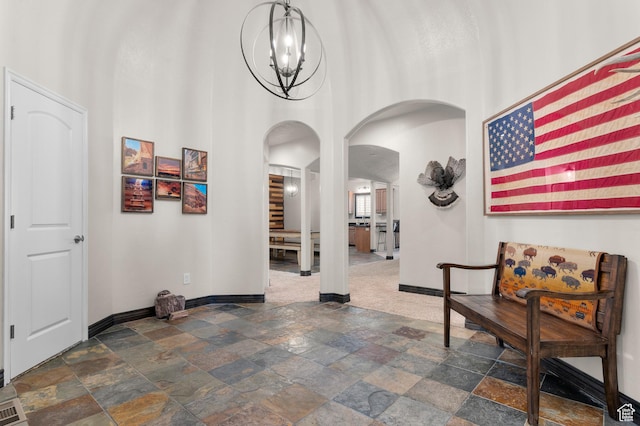 294 W Farmside Dr S, Saratoga Springs, UT 84045 - hallway featuring arched walkways, baseboards, stone tile flooring, a chandelier, and a high ceiling