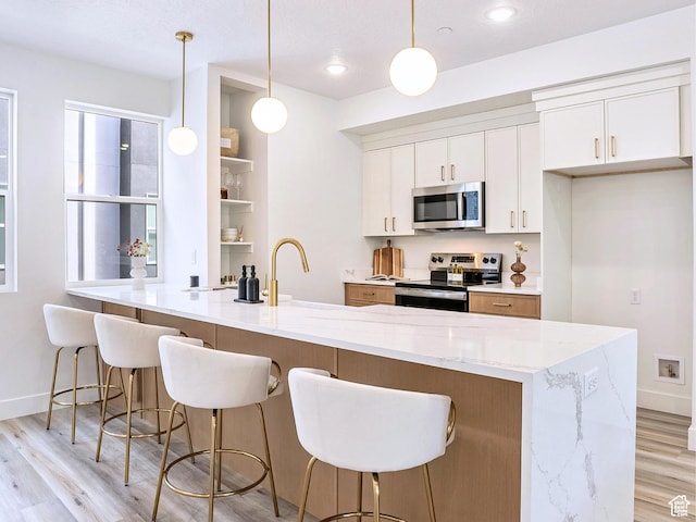 kitchen with baseboards, white cabinetry, light stone counters, light wood finished floors, and appliances with stainless steel finishes