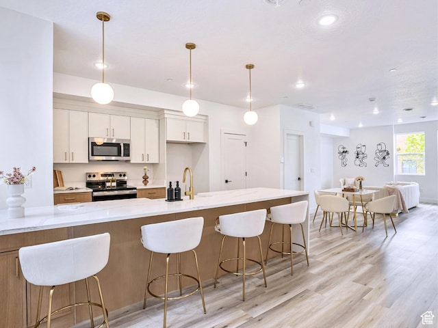 kitchen featuring open floor plan, a kitchen bar, white cabinets, light wood finished floors, and stainless steel appliances