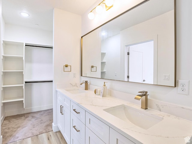 bathroom with double vanity, a sink, a walk in closet, and wood finished floors