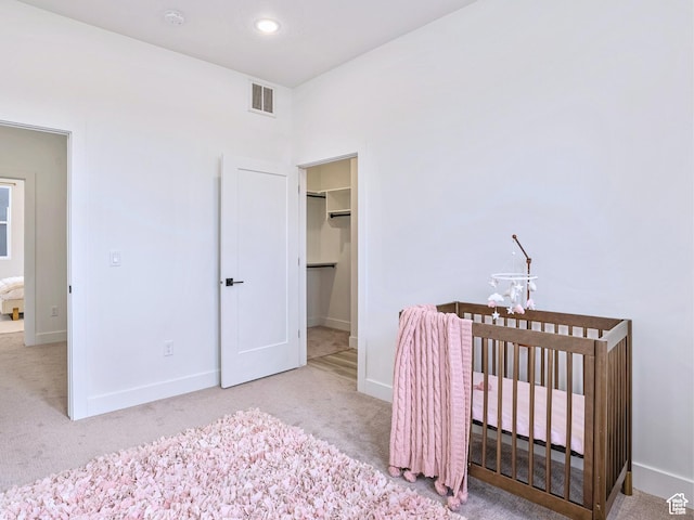 carpeted bedroom with baseboards, a nursery area, a spacious closet, and visible vents