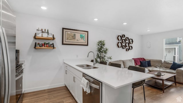 kitchen featuring a sink, stainless steel appliances, open floor plan, a peninsula, and light wood-type flooring