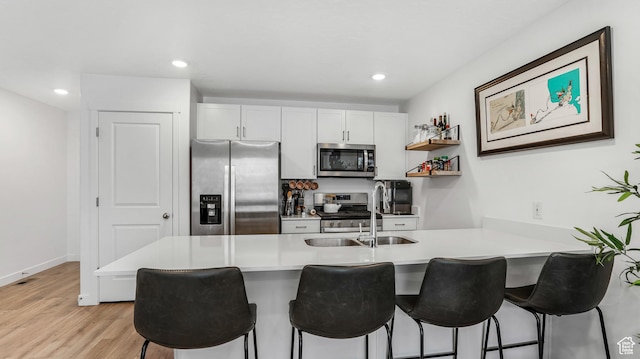 kitchen featuring a kitchen breakfast bar, appliances with stainless steel finishes, a sink, a peninsula, and light wood-style floors