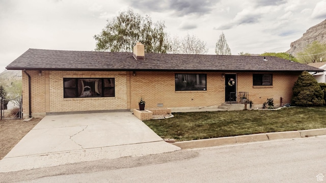 single story home featuring driveway, a chimney, a front yard, roof with shingles, and brick siding