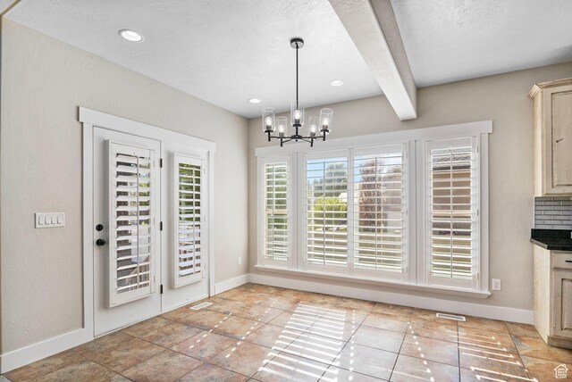 unfurnished dining area featuring baseboards, a chandelier, beam ceiling, and visible vents