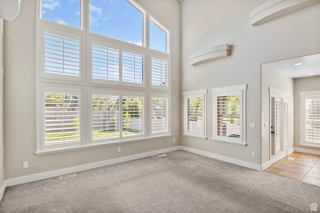 unfurnished living room with carpet floors, baseboards, plenty of natural light, and a high ceiling