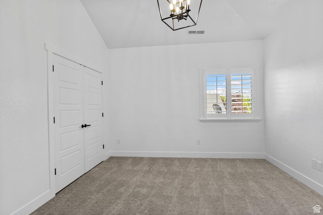 carpeted spare room with visible vents, baseboards, a chandelier, and vaulted ceiling