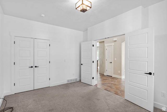 unfurnished bedroom featuring visible vents, baseboards, tile patterned floors, a closet, and carpet flooring