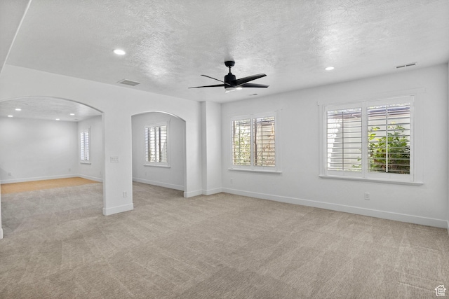 unfurnished living room with light colored carpet, arched walkways, a textured ceiling, a ceiling fan, and visible vents
