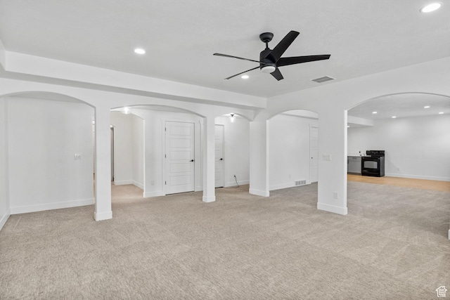 unfurnished living room with a ceiling fan, arched walkways, and light carpet