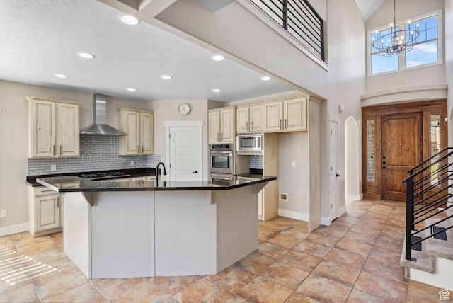 kitchen featuring wall chimney range hood, cream cabinets, arched walkways, stainless steel appliances, and baseboards