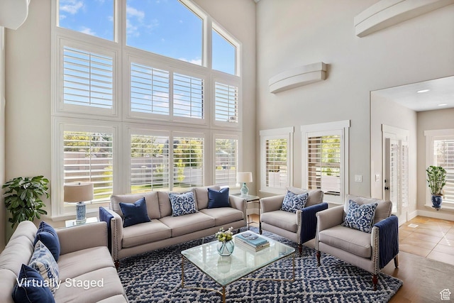 living area with baseboards, tile patterned floors, a high ceiling, and a wealth of natural light