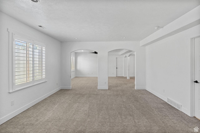 empty room featuring arched walkways, light carpet, a textured ceiling, and visible vents