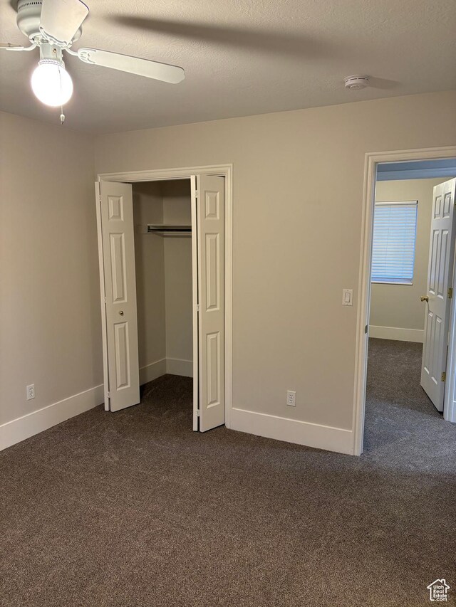 unfurnished bedroom with dark carpet, baseboards, ceiling fan, and a closet