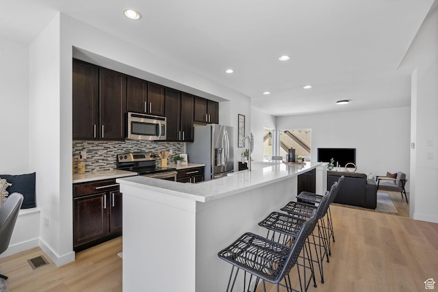 kitchen featuring appliances with stainless steel finishes, a breakfast bar, light wood finished floors, open floor plan, and backsplash